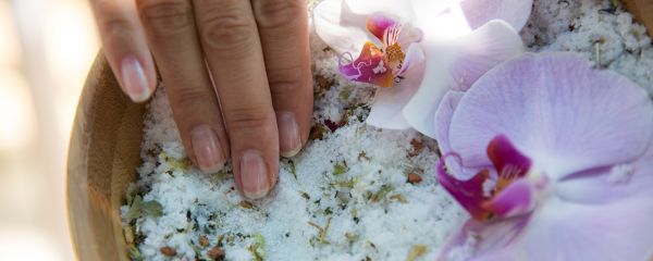 Hand in Peelingsalz mit Orchideenblüte