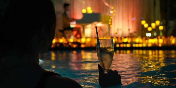 Person schwimmt in Wasser mit Getränk und schaut auf ein Klavier