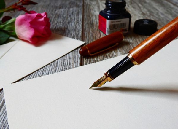 Blatt Papier auf einem Tisch mit einem Füller, Tinte und einer Rose daneben