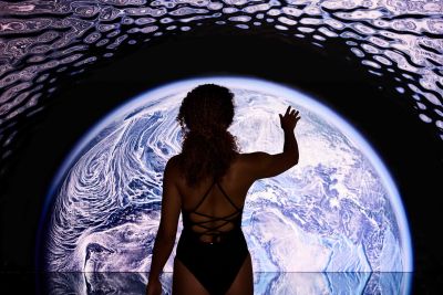 Eine Frau streckt ihre Hand nach der Erdkugel im Immersive Horizon aus