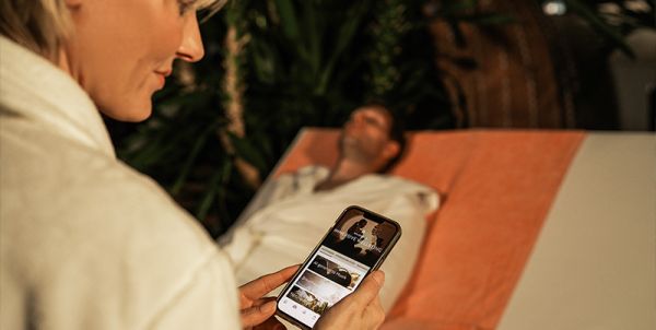 Hand hält Smartphone mit geöffneter App. In der Schrift steht: " BLUPHORIA-App - Der einfachste Weg in deine Lieblingstherme"