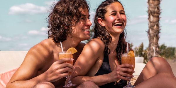 Zwei Personen sitzen lachend am Strand mit Cocktails in der Hand