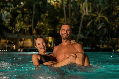 Ein Mann hebt eine Frau im Wasser hoch und sie lachen.