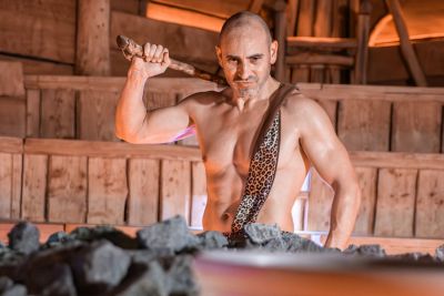 Mann in Höhlenmensch-Kostüm mit Keule in der Hand in einer Sauna.