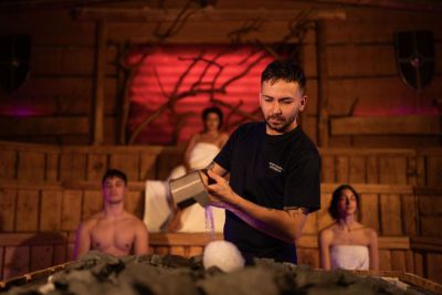 Mann gießt Wasser über eine Eiskugel in einer Sauna.