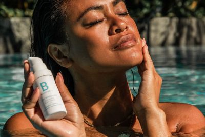 A woman is applying cream to her face whilst in the water.