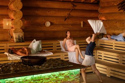 Several people are relaxing in a sauna whilst one person is waving a towel.