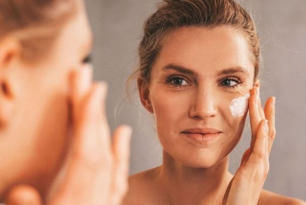 A woman is applying a face mask in front of a mirror.