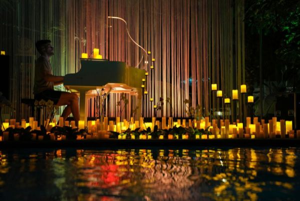 Mann spielt Piano umgeben von Wasser und Kerzen.